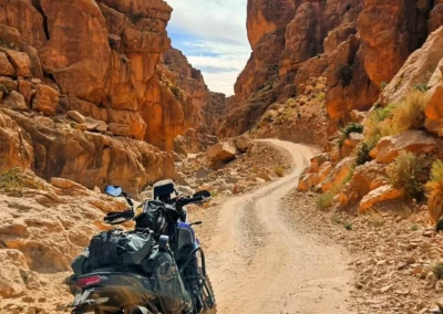 Adventure motorcycle on a winding dirt track inside a narrow red-rock canyon in Morocco.