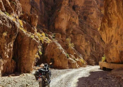 Adventure motorcycle riding through a narrow rocky canyon in Morocco.