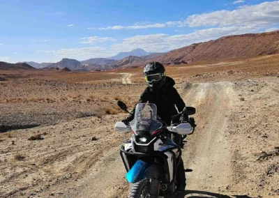 ADV rider on a dirt track crossing a wide rocky desert plain in Morocco.