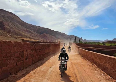 Group of ADV riders on a dusty dirt road between clay walls in the Moroccan mountains.