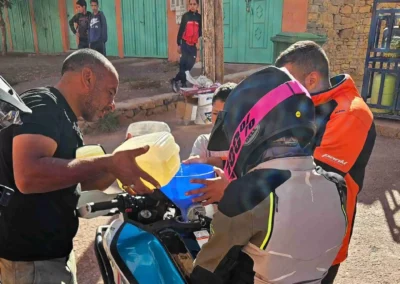 Local men helping an ADV rider refuel a motorcycle from jerrycans in a Moroccan village.