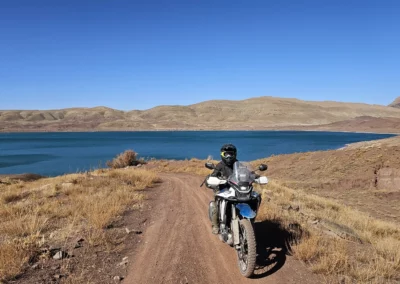 ADV rider on a dirt track overlooking a large blue lake in the Moroccan mountains.