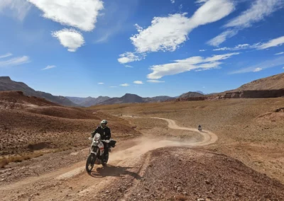 ADV riders following a winding dirt trail through a wide rocky desert valley in Morocco.