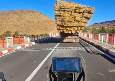 View from an ADV motorcycle following an overloaded hay truck on a mountain road in Morocco.