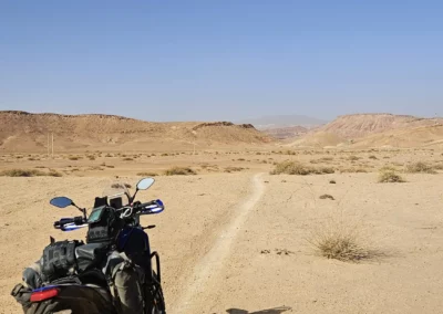 Adventure motorcycle on a narrow trail crossing a wide barren desert plain in Morocco.