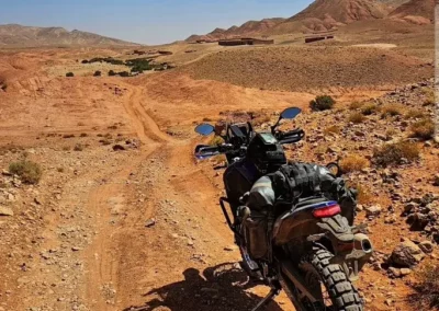 Adventure motorcycle parked on a rocky dirt track overlooking a dry desert valley in Morocco.