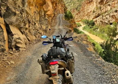 Adventure motorcycle on a narrow cliffside dirt track in a Moroccan canyon.