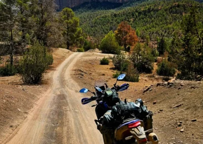 Adventure motorcycle on a dirt track in Morocco, with a large cliff and forest in the background.