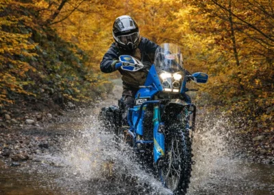 Adventure motorcycle crossing a shallow river on a forest trail in the Balkans during autumn.