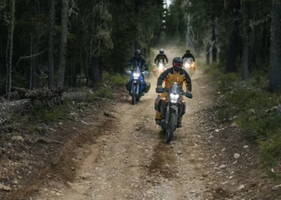 A group of adventure motorcycles riding an off-road forest track in the Balkan mountains.