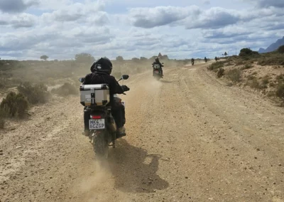 Group of adventure riders travelling along a dusty gravel road in South Africa.